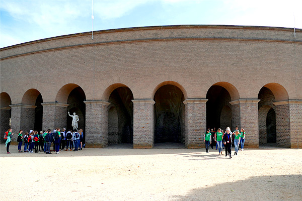 SchülerInnengruppen vor der wiederaufgebauten Arena mit der Statur des Kaisers Trajan.